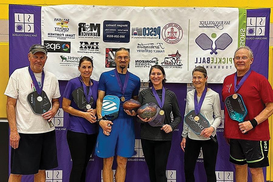 Group of individuals with their medals and their pickleball paddles.