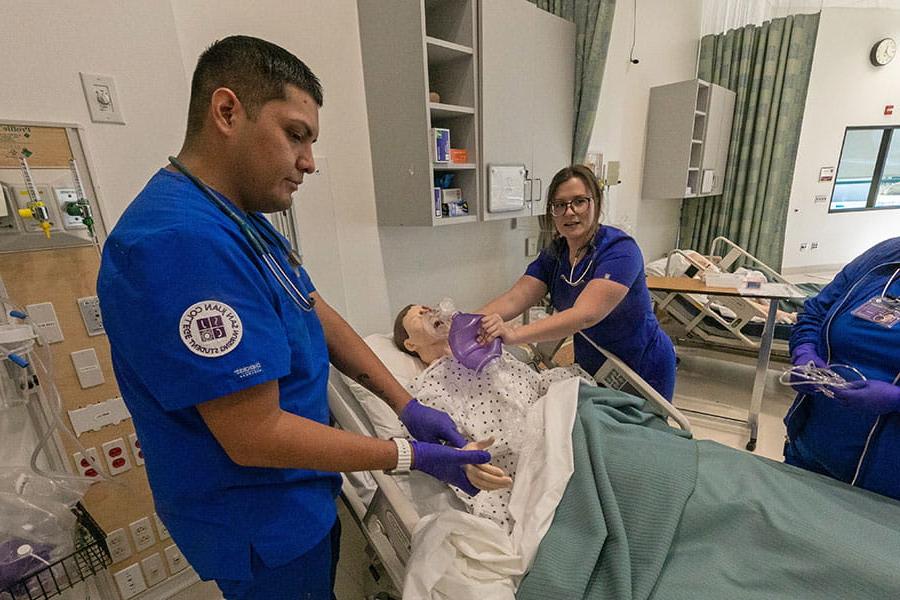 Nursing students practice patient care with medical dummy.